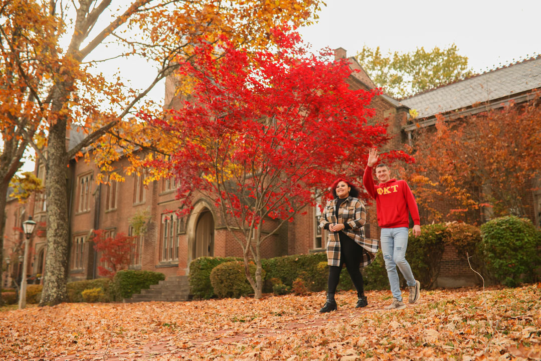 students waving in fall leaves